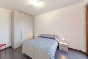 Une chambre à coucher avec un lit, des tables de chevet, une armoire et un fauteuil rouge.