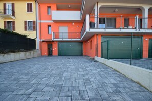 A multi-story building with a flat roof, a paved courtyard, and a green garage door.