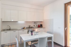 Cocina compacta con armarios blancos, estufa a gas, cafetera y una mesa de comedor con sillas.