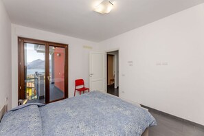 A bedroom with a bed, a red chair, and a door leading to a balcony with a view.