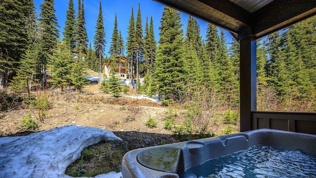 A hot tub with a snowy ground in front, surrounded by tall pine trees and a wooden deck. - Upscale Ski In/Out Duplex on The Ridge with Garage, Private Hot Tub, laundry (Silver Star Mountain)