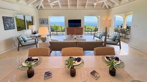 A spacious living area with a high ceiling, a central seating arrangement, and large windows offering a view of the outdoors.