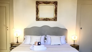 A large bed with a grey headboard, white bedding, and two bedside tables with lamps. A mirror hangs on the wall above the bed.
