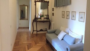 A hallway with a wooden floor leading to a room with a sofa, a mirror, and framed pictures on the wall.