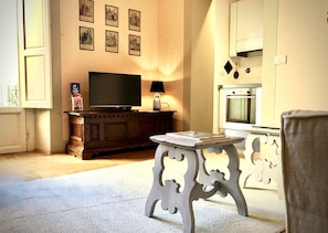 Uma sala de estar com televisão sobre um aparador de madeira, uma mesa pequena e uma cadeira.