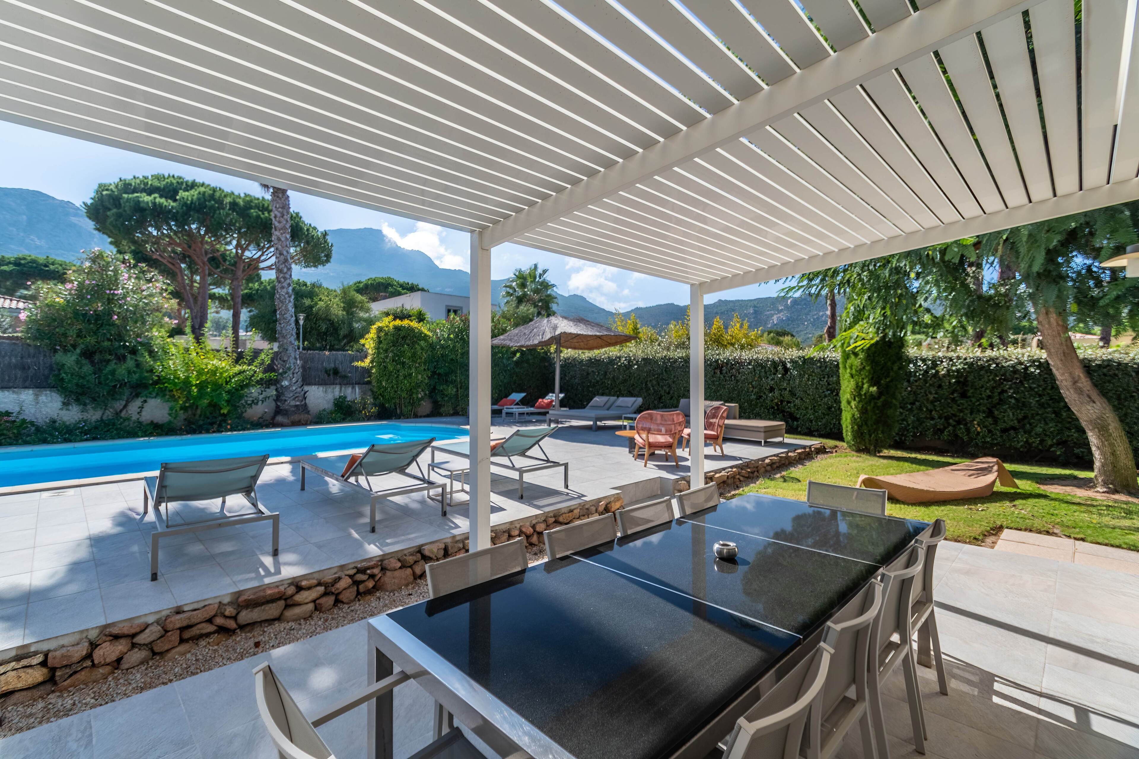 An outdoor pool area with a pergola, lounge chairs, and a dining table.