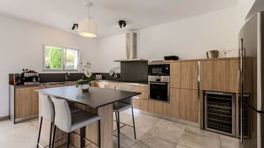 Une cuisine moderne dotée d’un îlot central, de meubles en bois, d’appareils électroménagers en acier inoxydable et d’une fenêtre laissant entrer la lumière naturelle.