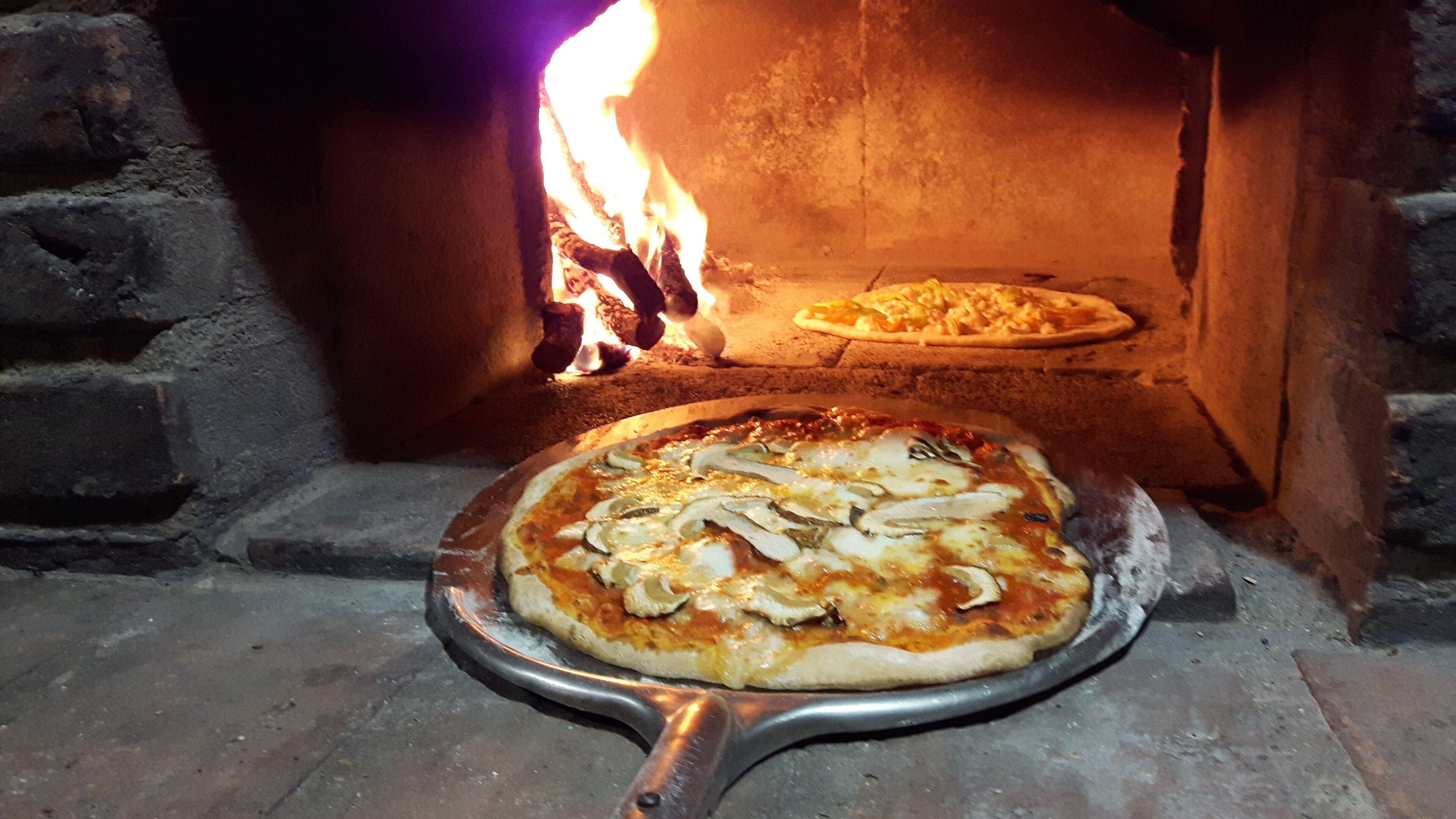 Un horno de pizza con una pizza sobre una bandeja metálica frente a él.