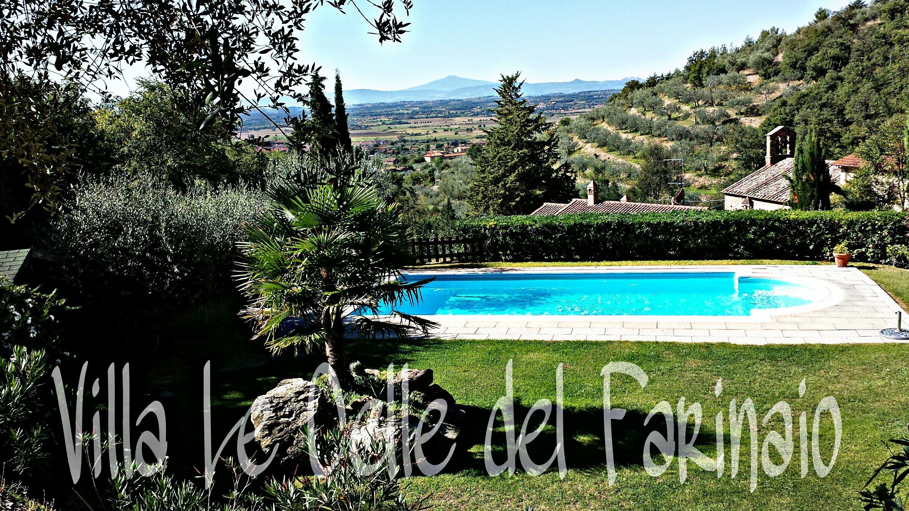 Villa Le Volte del Parinò with a swimming pool, surrounded by lush greenery and a view of distant hills.