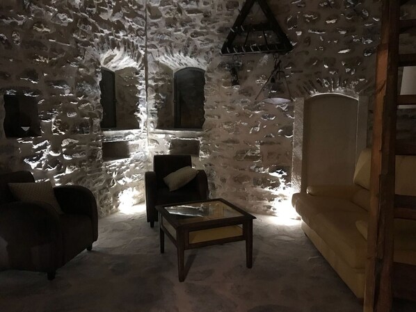 A cozy room with a stone wall, a wooden sofa, a small table, and a chair.
