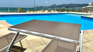 Piscina con vistas a montañas, zona de estar cubierta y terraza amurallada.