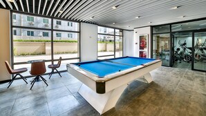Une table de billard avec des chaises, de grandes fenêtres et des vélos d’exercice.