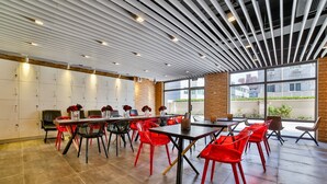 Une salle de conférence moderne, dotée d’une longue table, de chaises rouges et noires, et d’un mur en briques.
