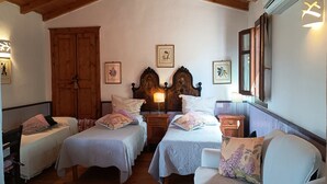 Un dormitorio acogedor con dos camas individuales, cabecero de madera, mesitas de noche con lámparas y cuadros con motivos florales en las paredes.