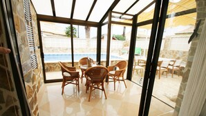 Ein überdachter Patio mit Blick auf den Pool, ausgestattet mit Korbmöbeln und Steinwänden.
