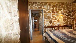 Ein Schlafzimmer mit Steinwand, einem Bett mit gemustertem Überwurf und einem hölzernen Kopfteil.