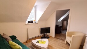 A living room with a green sofa, a white armchair, a TV, and a small table with remotes. - Apartment with terrace and best conditions for restful sleep (Dahme)