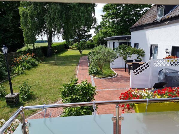 A garden view with a paved pathway, a white building, and a table with chairs.