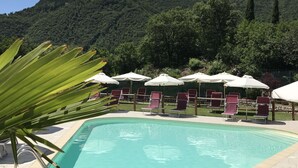 A swimming pool with lounge chairs and umbrellas, surrounded by greenery and a mountainous backdrop. - Residence Garden: Three-room apartment with garden                            (Tignale)