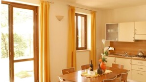 A dining area with a wooden table and chairs, a vase with flowers, and a kitchen in the background. - Residence Garden: Three-room apartment with garden                            (Tignale)