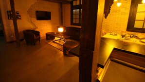 Um quarto com pouca luz, parede de tijolos, um banco de madeira, uma pequena mesa e uma janela com vista para o exterior.