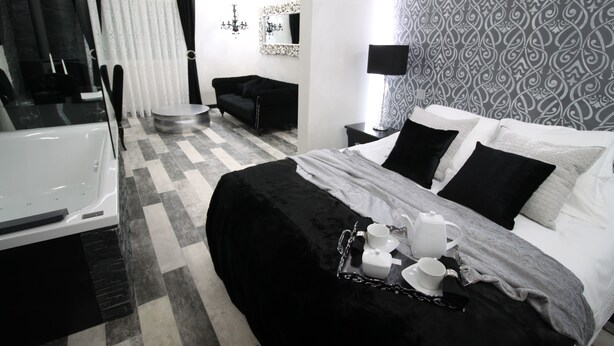 Een moderne hotelkamer met een geruite vloer, een zwart-wit gestreepte wand, een zwarte bank, een bed met zwart-wit beddengoed, en een dienblad met witte kopjes en schotels.
