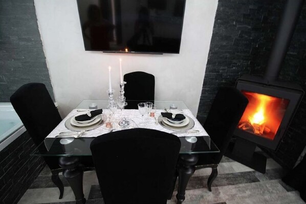 Un coin repas avec une table dressée pour deux personnes, un téléviseur à écran plat fixé au mur au-dessus, et une cheminée sur le côté droit.
