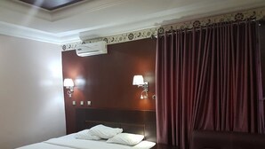 A hotel room with a bed, bedside lamps, an air conditioner, and a dark-colored sofa. - Grand Valley Hotel (Abuja)