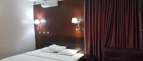 Een hotelkamer met een bed, nachtlampjes, een airconditioner en een donkergroene bank.