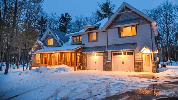 Une maison à deux étages avec un garage, entourée d’un paysage enneigé et d’arbres.