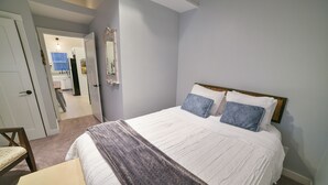 Une chambre à coucher comprenant un lit, une table de chevet, une chaise et une porte donnant sur une salle de bain.