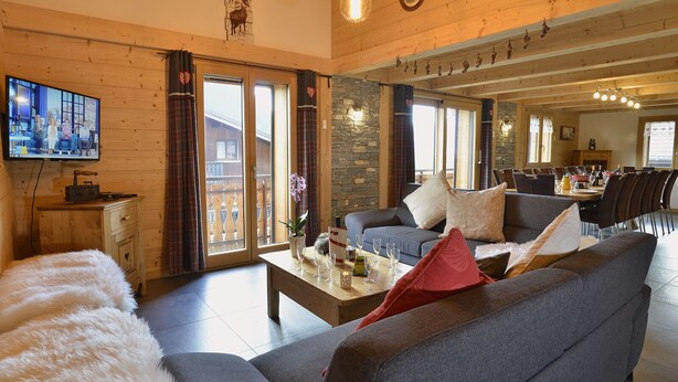 Ett rymligt vardagsrum med en grå soffa, ett soffbord i trä och en tv som är monterad på väggen.
