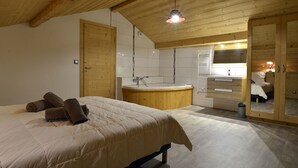 Ett sovrum med en stor säng, ett träpanelat tak, ett inbyggt badkar och en trägarderob.