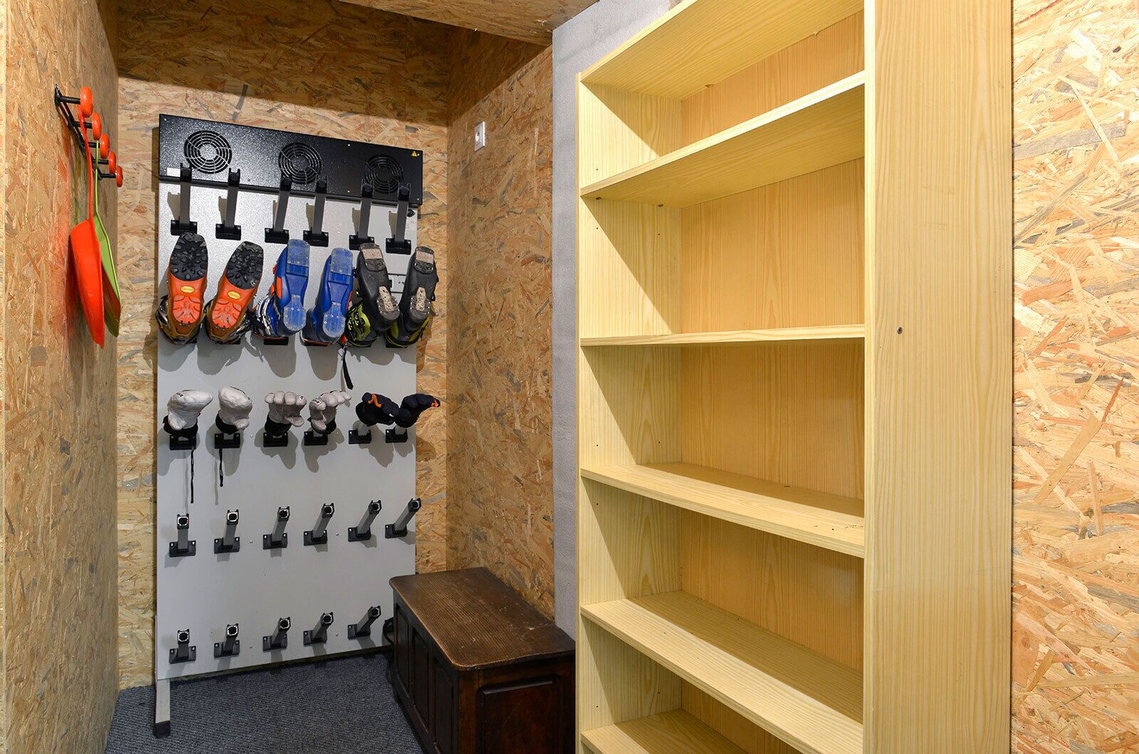 A room with a shoe rack holding various types of footwear, a small wooden table, and a wooden shelving unit.