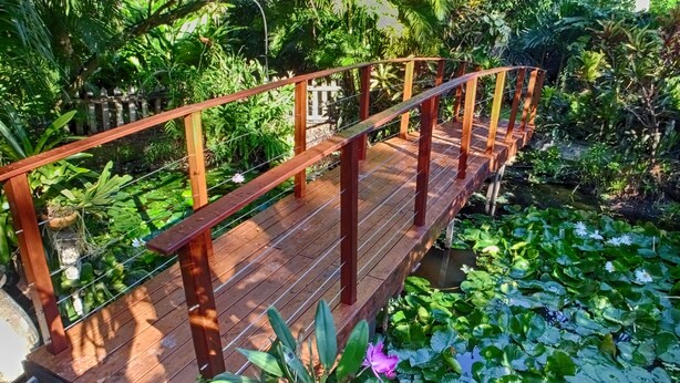 A wooden bridge over a pond with lily pads and water lilies.