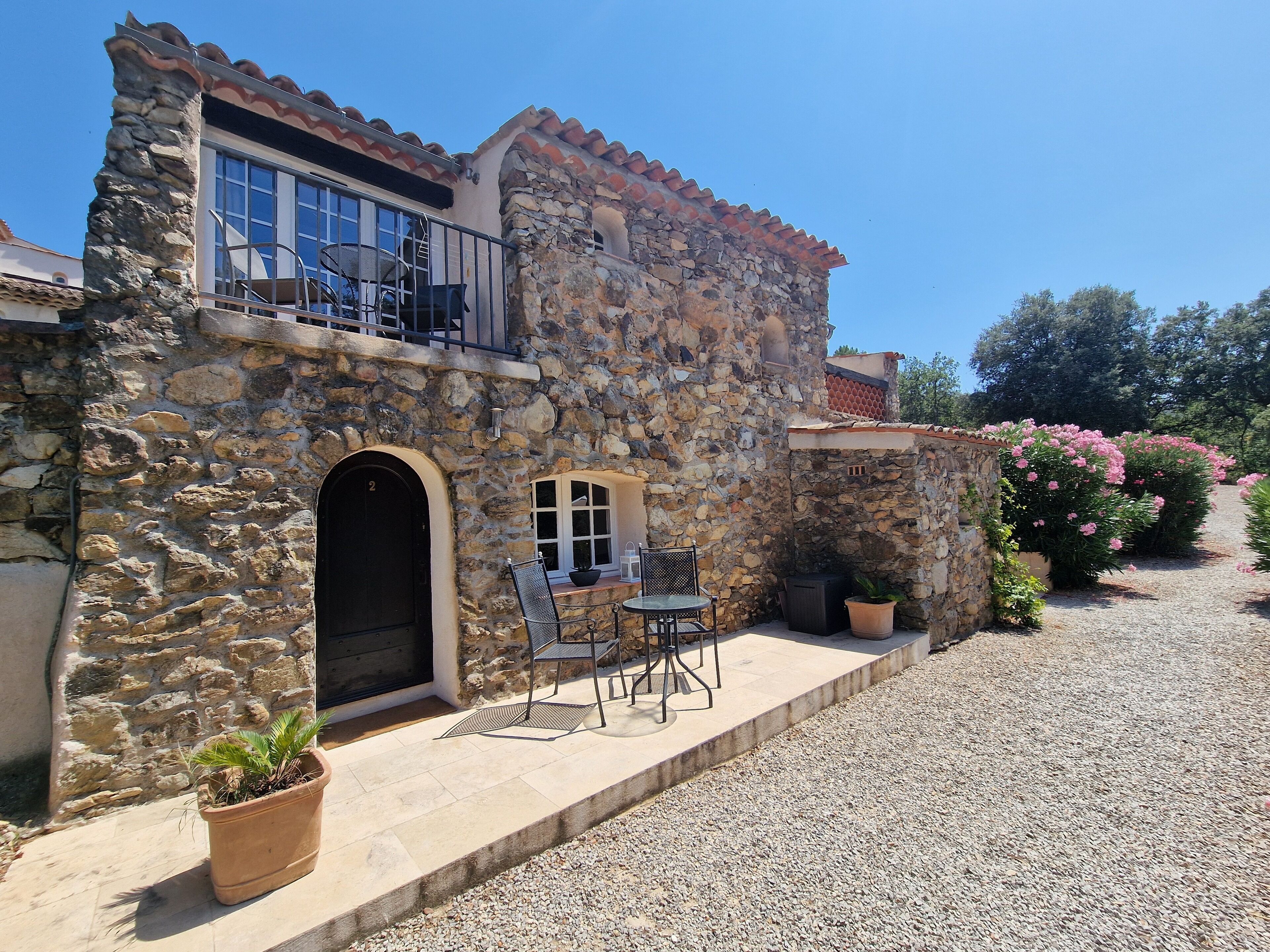 Un edificio de piedra con balcón, una puerta y un pequeño patio con mesa y sillas.