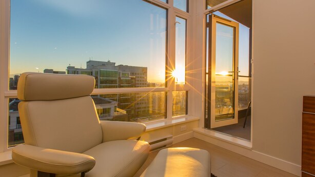 A modern living room with a large window, a sofa, and a small ottoman. - EraBella-Downtown 12th floor Beauty, Free Parking and Wifi, Close to Everything by Victoria Prime! (Victoria)