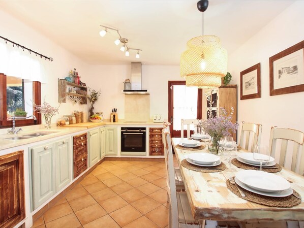 A kitchen with a dining area, featuring a wooden table set for two, a built-in oven, and a hanging light fixture.