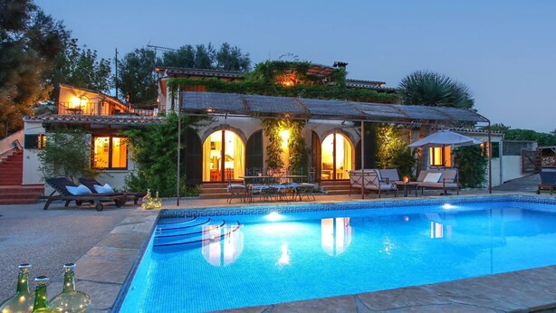 A poolside area with a swimming pool, lounge chairs, and a building with arched windows and outdoor lighting.