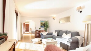 A living room with a grey sofa, a red armchair, a coffee table, and a dining area with a wooden table and chairs.