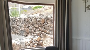 A dining area with a round glass table, four chairs, a bowl, and a view of a rocky outdoor landscape through a window. - Amazing panoramic sea views!!!  (Playa Blanca)