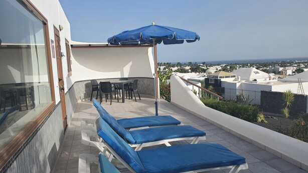 A rooftop terrace with blue lounge chairs, a table with chairs, and a blue umbrella. - Amazing panoramic sea views!!!  (Playa Blanca)
