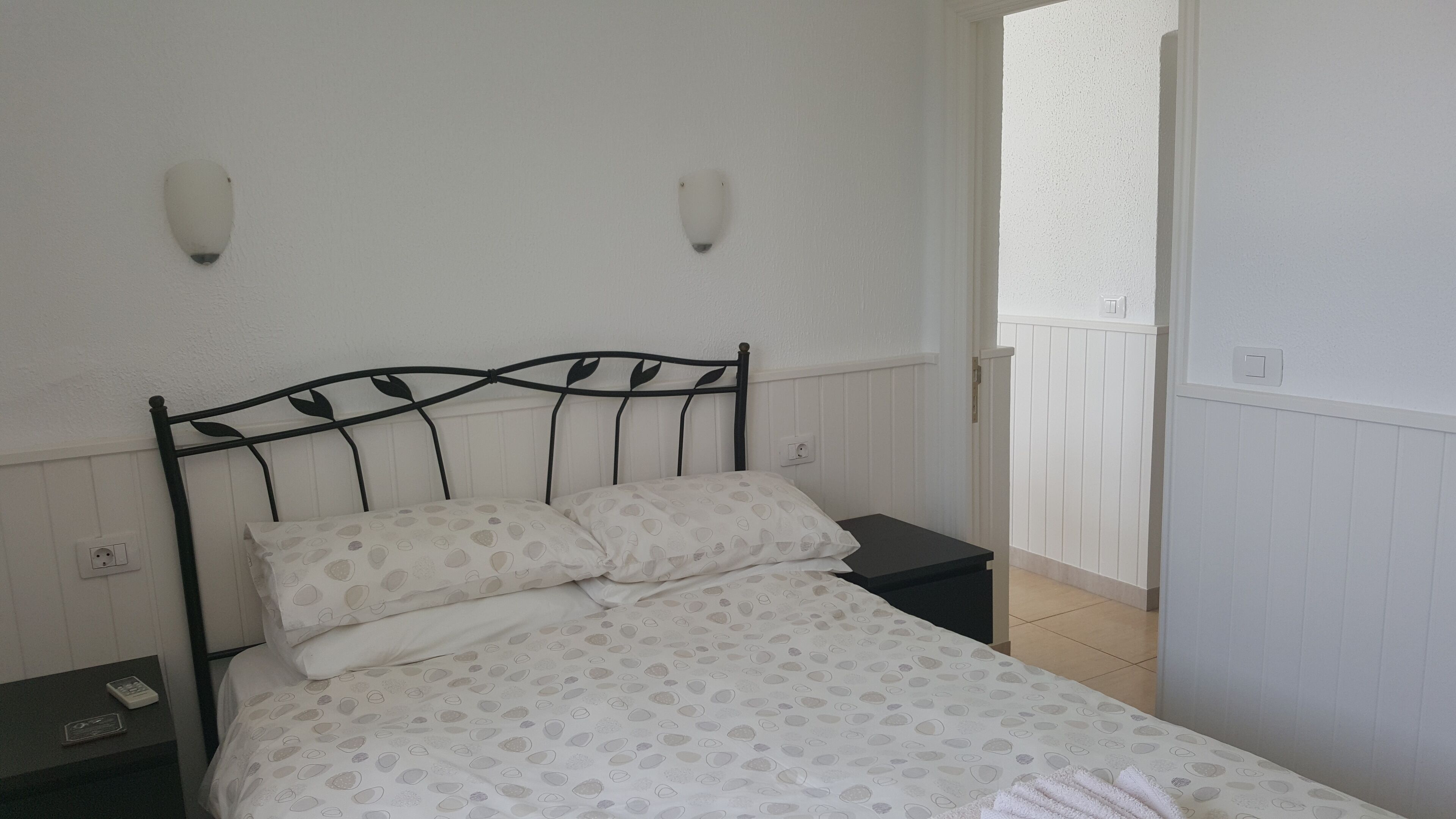 A neatly made bed with a patterned bedspread, a black metal headboard, and two wall-mounted light fixtures.