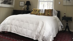 A bedroom with a large bed, a window, a ceiling fan, and a wall-mounted lamp.