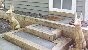 A wooden staircase leading to a house with two sculptures of rabbits on the steps.