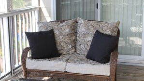 Een rieten bank met gekleurde kussens op een houten terras.
