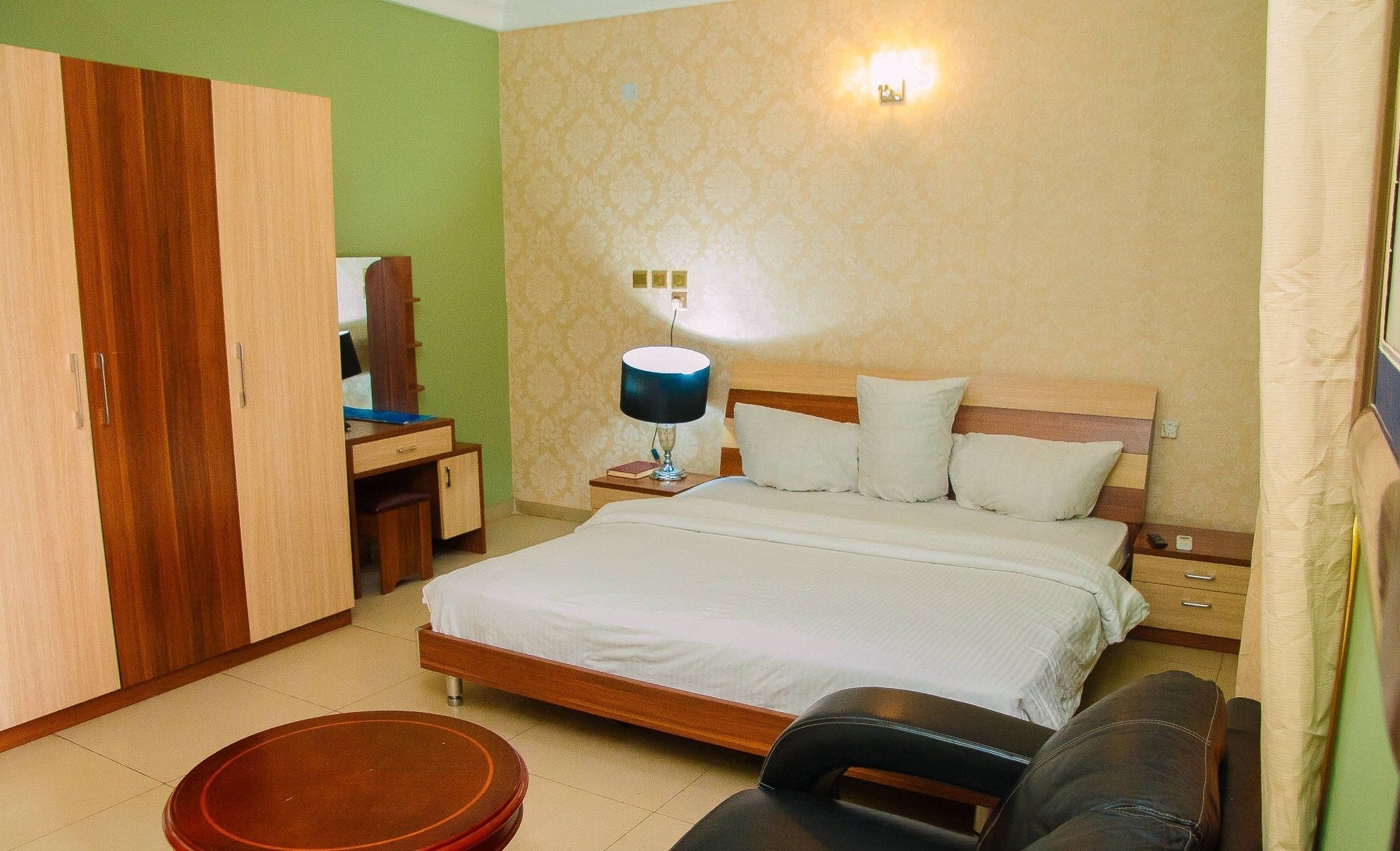 A bedroom with a bed, bedside table, lamp, wardrobe, and a small round table.