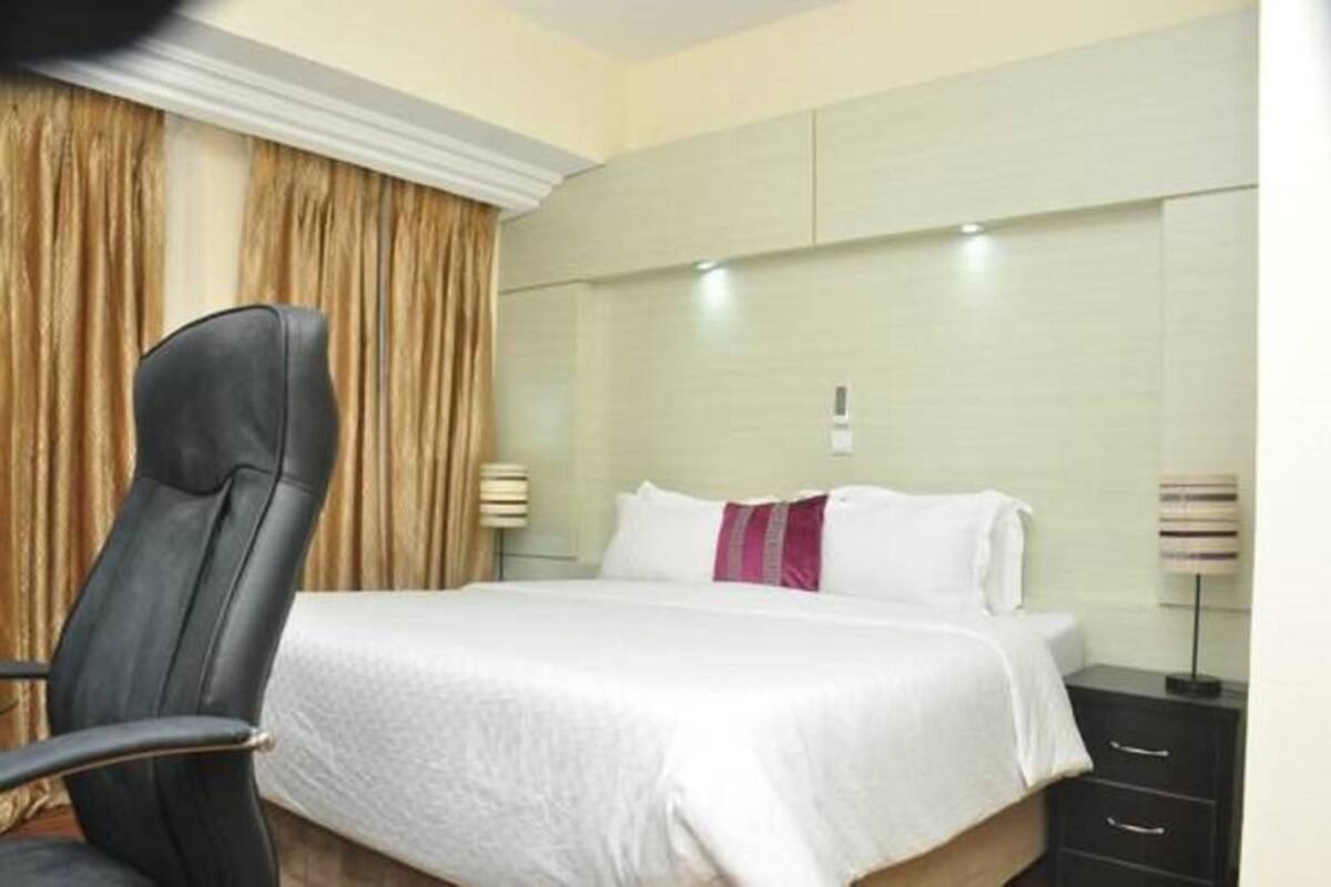 Een hotelkamer met een bed, een stoel, een nachtkastje en een lamp.