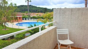 A balcony with a white chair, a pool, and a view of a residential area with houses and trees. - Le lavandou, lovely small air-conditioned mazet 3 minutes from the beach and shops (Le Lavandou)