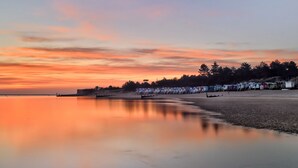 A beach with a row of beach huts and a calm sea at sunset. - Oyster Cottage, Wells-next-the-Sea, Norfolk (Wells Next the Sea)